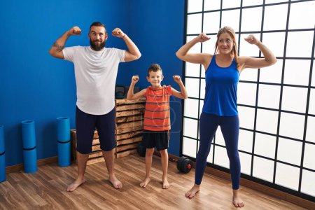 Foto de Familia de tres usando ropa deportiva en el gimnasio sonriendo mirando hacia un lado y mirando hacia otro pensando. - Imagen libre de derechos