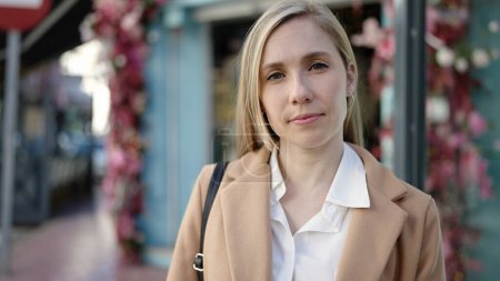 Téléchargez les photos : Jeune femme blonde debout avec une expression sérieuse à la terrasse du café - en image libre de droit