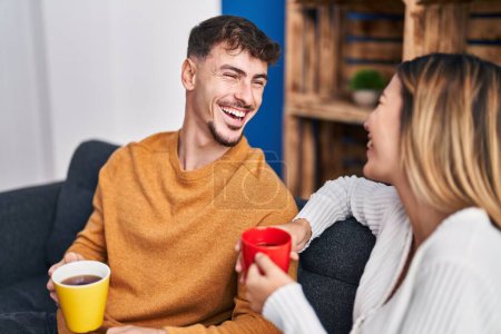 Photo for Young man and woman couple drinking coffee sitting on sofa at home - Royalty Free Image