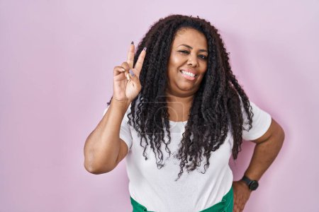 Photo for Plus size hispanic woman standing over pink background smiling looking to the camera showing fingers doing victory sign. number two. - Royalty Free Image