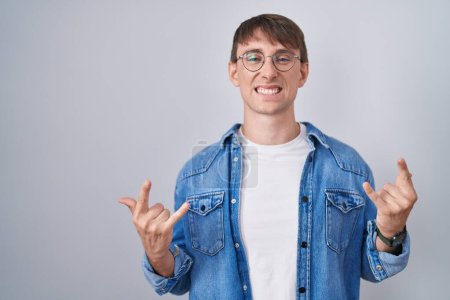 Photo for Caucasian blond man standing wearing glasses shouting with crazy expression doing rock symbol with hands up. music star. heavy music concept. - Royalty Free Image
