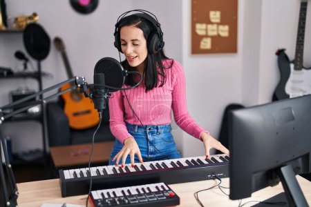 Foto de Joven mujer caucásica músico cantando canción tocando el piano en el estudio de música - Imagen libre de derechos