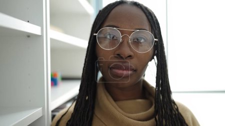Téléchargez les photos : Femme africaine debout avec une expression sérieuse portant des lunettes à l'université de la bibliothèque - en image libre de droit