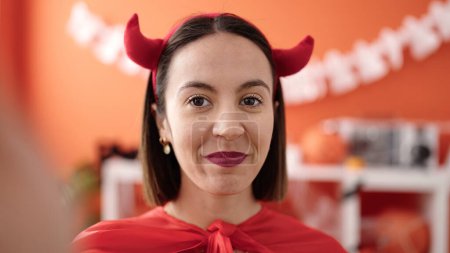 Téléchargez les photos : Young beautiful hispanic woman wearing devil costume make selfie by camera at home - en image libre de droit