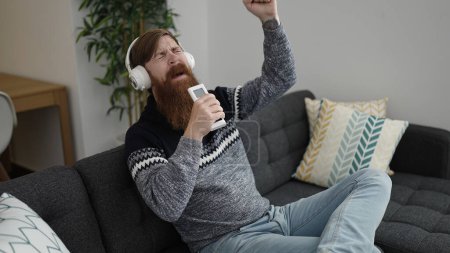 Téléchargez les photos : Young redhead man listening to music singing song at home - en image libre de droit