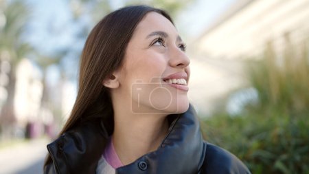 Foto de Joven hermosa mujer hispana sonriendo confiada mirando al cielo en el parque - Imagen libre de derechos