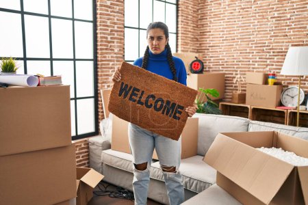 Photo for Young hispanic woman holding welcome doormat at new home skeptic and nervous, frowning upset because of problem. negative person. - Royalty Free Image