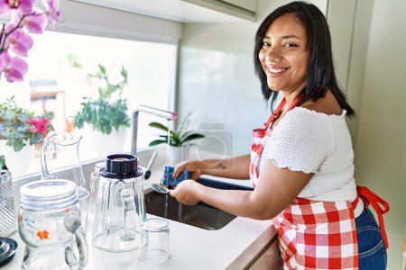 Téléchargez les photos : Hispanique brune femme lave la vaisselle à la cuisine - en image libre de droit