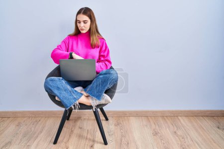Téléchargez les photos : Jeune fille hispanique travaillant à l'aide d'un ordinateur portable en vérifiant l'heure sur la montre-bracelet, détendu et confiant - en image libre de droit