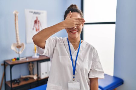 Photo for Young hispanic woman working at rehabilitation clinic smiling and laughing with hand on face covering eyes for surprise. blind concept. - Royalty Free Image