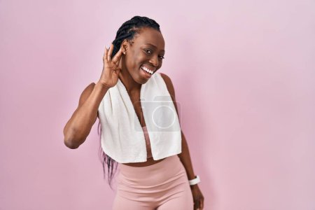 Photo for Beautiful black woman wearing sportswear and towel over pink background smiling with hand over ear listening an hearing to rumor or gossip. deafness concept. - Royalty Free Image