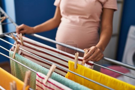 Foto de Mujer latina joven embarazada colgando ropa en tendedero en la sala de lavandería - Imagen libre de derechos