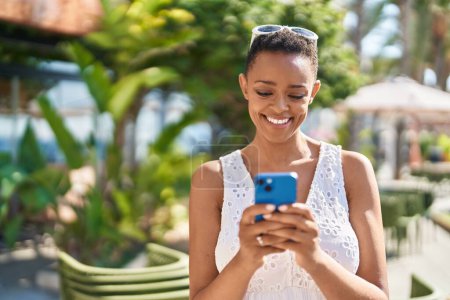 Foto de Mujer afroamericana sonriendo confiada usando smartphone en el parque - Imagen libre de derechos