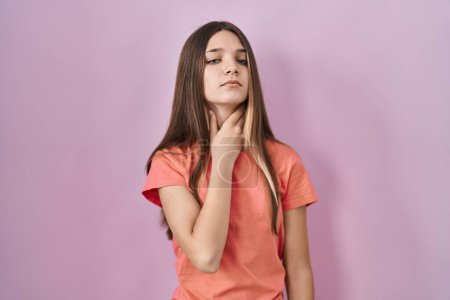Foto de Chica adolescente de pie sobre fondo rosa tocando el cuello doloroso, dolor de garganta para la gripe, la clod y la infección - Imagen libre de derechos