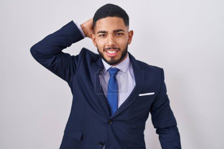 Téléchargez les photos : Jeune homme hispanique portant costume d'affaires et cravate souriant confiant toucher les cheveux avec geste de la main vers le haut, posant attrayant et à la mode - en image libre de droit