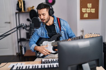Téléchargez les photos : Jeune homme hispanique chantant une chanson jouant de la guitare électrique au studio de musique - en image libre de droit