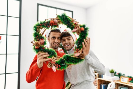 Téléchargez les photos : Deux hommes hispaniques couple étreignant l'autre tenant décor de Noël à la maison - en image libre de droit