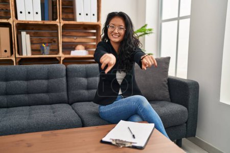Photo for Young asian woman at consultation office pointing to you and the camera with fingers, smiling positive and cheerful - Royalty Free Image