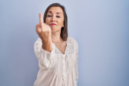 Foto de Middle age hispanic woman standing over blue background showing middle finger, impolite and rude fuck off expression - Imagen libre de derechos