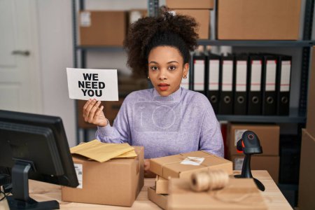 Téléchargez les photos : Jeune femme afro-américaine travaillant dans un commerce électronique de petite entreprise tenant une bannière effrayée et étonnée avec la bouche ouverte pour la surprise, visage incrédule - en image libre de droit