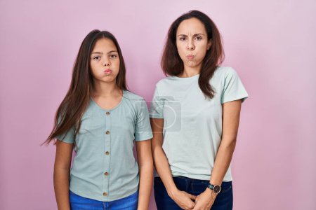 Photo for Young mother and daughter standing over pink background puffing cheeks with funny face. mouth inflated with air, crazy expression. - Royalty Free Image