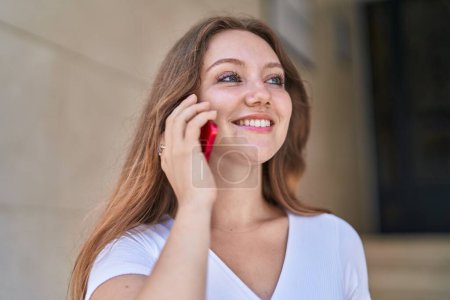 Foto de Mujer rubia joven sonriendo confiada hablando en el teléfono inteligente en la calle - Imagen libre de derechos