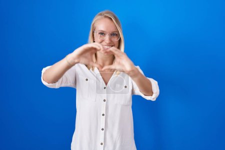 Photo for Young caucasian woman standing over blue background smiling in love doing heart symbol shape with hands. romantic concept. - Royalty Free Image
