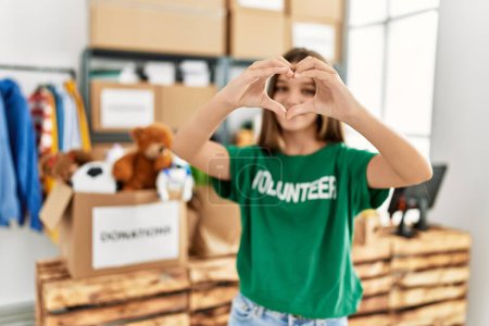 Téléchargez les photos : Adorable fille portant un uniforme bénévole faisant symbole du cœur avec les mains au centre de charité - en image libre de droit