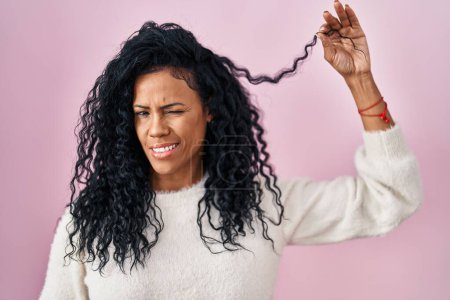Téléchargez les photos : Moyen Age femme hispanique tenant les cheveux bouclés clin d'oeil en regardant la caméra avec une expression sexy, gai et heureux visage. - en image libre de droit