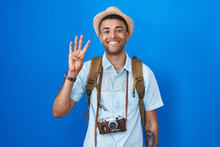 Photo for Brazilian young man holding vintage camera showing and pointing up with fingers number four while smiling confident and happy. - Royalty Free Image