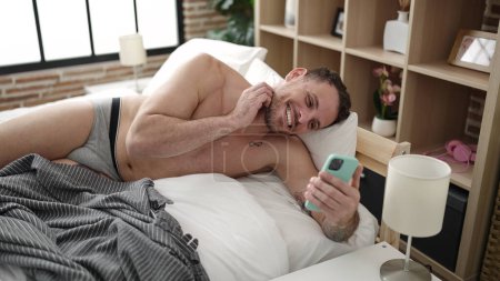 Photo for Young caucasian man doing video call with smartphone lying on the bed at bedroom - Royalty Free Image