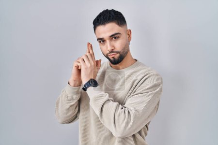 Photo for Young handsome man standing over isolated background holding symbolic gun with hand gesture, playing killing shooting weapons, angry face - Royalty Free Image