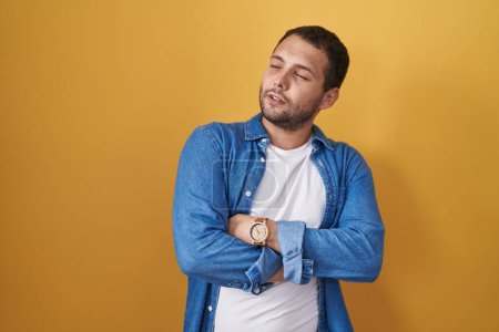 Téléchargez les photos : Hispanic man standing over yellow background looking to the side with arms crossed convinced and confident - en image libre de droit