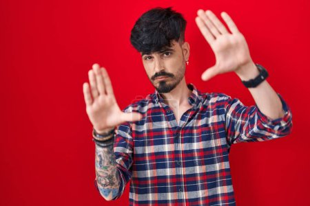 Photo for Young hispanic man with beard standing over red background doing frame using hands palms and fingers, camera perspective - Royalty Free Image