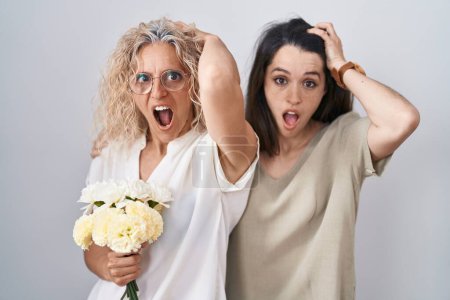 Téléchargez les photos : Mère et fille tenant un bouquet de fleurs blanches folles et effrayées avec les mains sur la tête, effrayées et surprises de choc avec la bouche ouverte - en image libre de droit