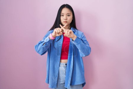 Photo for Young asian woman standing over pink background rejection expression crossing fingers doing negative sign - Royalty Free Image