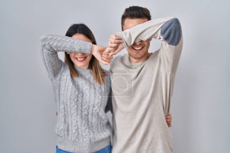 Foto de Young hispanic couple standing over white background smiling cheerful playing peek a boo with hands showing face. surprised and exited - Imagen libre de derechos