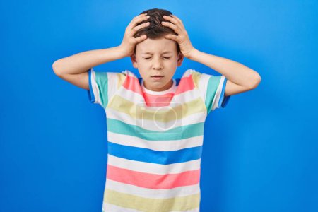 Téléchargez les photos : Jeune enfant caucasien debout sur fond bleu souffrant de maux de tête désespérés et stressés parce que la douleur et la migraine. mains sur la tête. - en image libre de droit