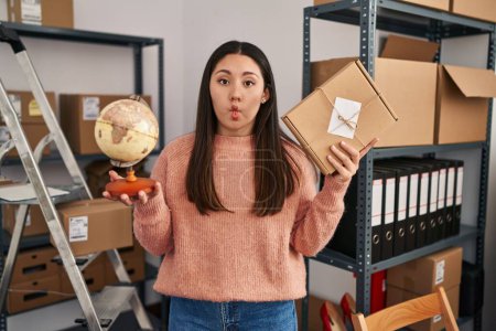 Photo for Young latin woman working at small business ecommerce doing world shipping making fish face with mouth and squinting eyes, crazy and comical. - Royalty Free Image