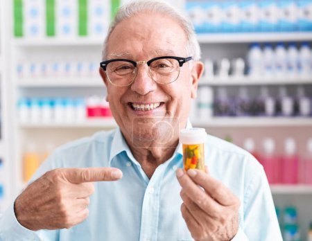 Téléchargez les photos : Homme âgé aux cheveux gris tenant des pilules à la pharmacie souriant heureux pointant avec la main et le doigt - en image libre de droit