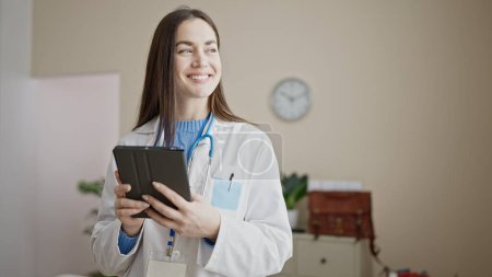 Téléchargez les photos : Jeune femme caucasienne médecin en utilisant touchpad à la clinique - en image libre de droit