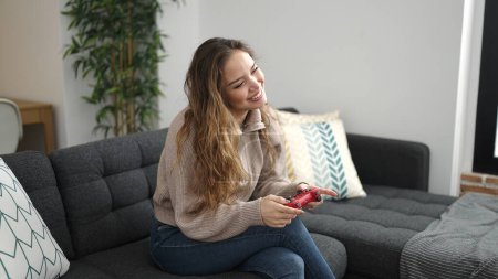 Foto de Joven mujer hispana hermosa jugando videojuego sentado en el sofá en casa - Imagen libre de derechos