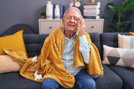 Foto de Hombre de pelo gris de mediana edad que sufre de dolor de cabeza sentado en el sofá en casa - Imagen libre de derechos