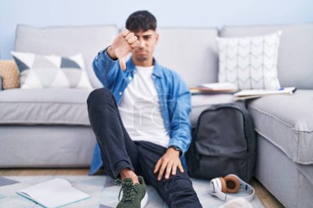 Photo for Young hispanic man sitting on the floor studying for university looking unhappy and angry showing rejection and negative with thumbs down gesture. bad expression. - Royalty Free Image