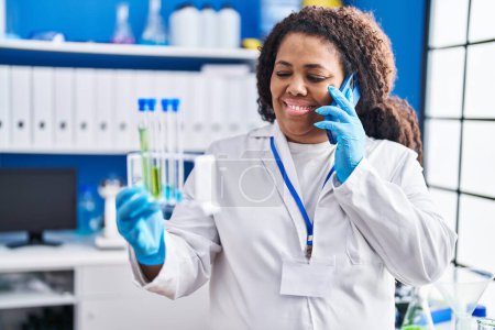 Photo for African american woman scientist talking on smartphone holding test tubes at laboratory - Royalty Free Image