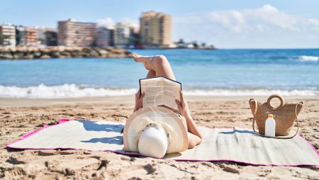 Photo for Young hispanic woman wearing bikini and summer hat reading book at seaside - Royalty Free Image
