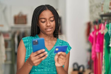 Foto de Cliente afroamericano usando smartphone y tarjeta de crédito en tienda de ropa - Imagen libre de derechos