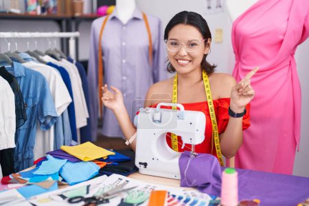 Photo for Hispanic young woman dressmaker designer using sewing machine smiling confident pointing with fingers to different directions. copy space for advertisement - Royalty Free Image