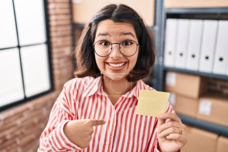 Photo for Young hispanic woman holding paper reminder at the office pointing finger to one self smiling happy and proud - Royalty Free Image