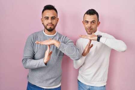 Photo for Homosexual couple standing over pink background doing time out gesture with hands, frustrated and serious face - Royalty Free Image